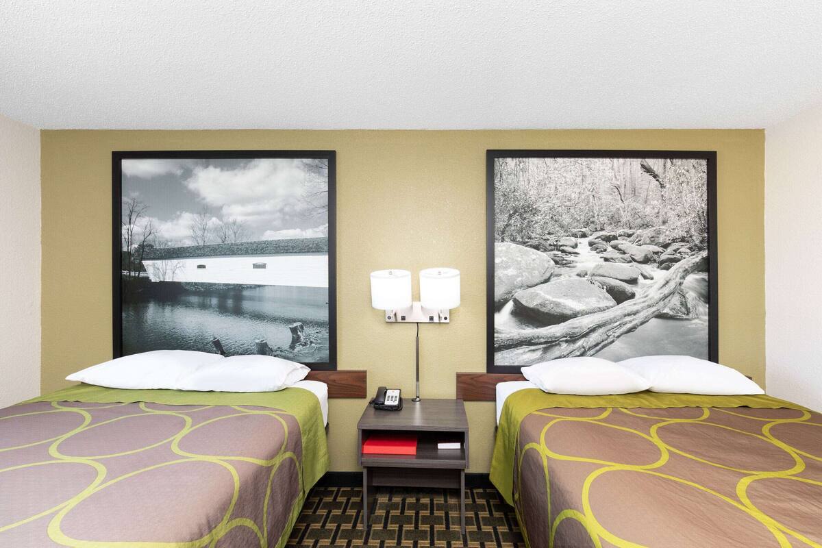 A hotel room with two beds, a nightstand with a phone, and two wall-mounted lamps.