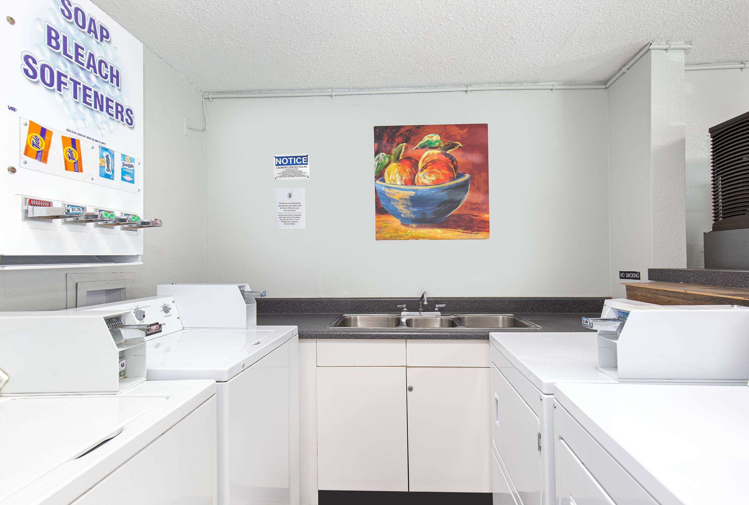 A kitchen with white appliances, a painting of fruit, and a notice sign.