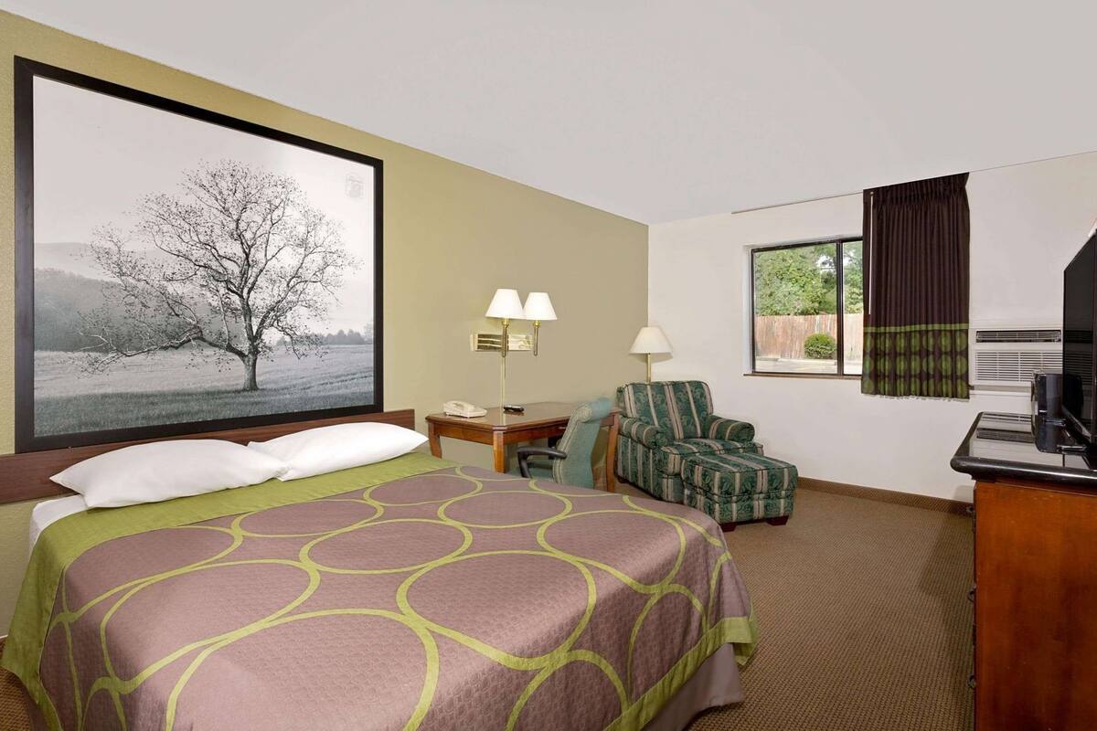 A hotel room with a bed, a desk, a chair, a television, and a window with curtains.