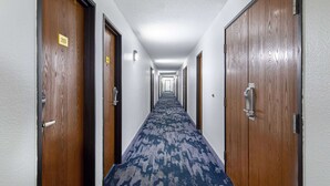 A hotel hallway with wooden doors, numbered room signs, and a patterned carpet.