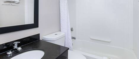 A bathroom with a black countertop sink, a white toilet, and a white bathtub.