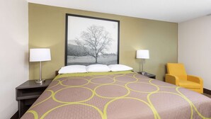 A hotel room with a bed, two bedside lamps, a chair, and a framed picture on the wall.