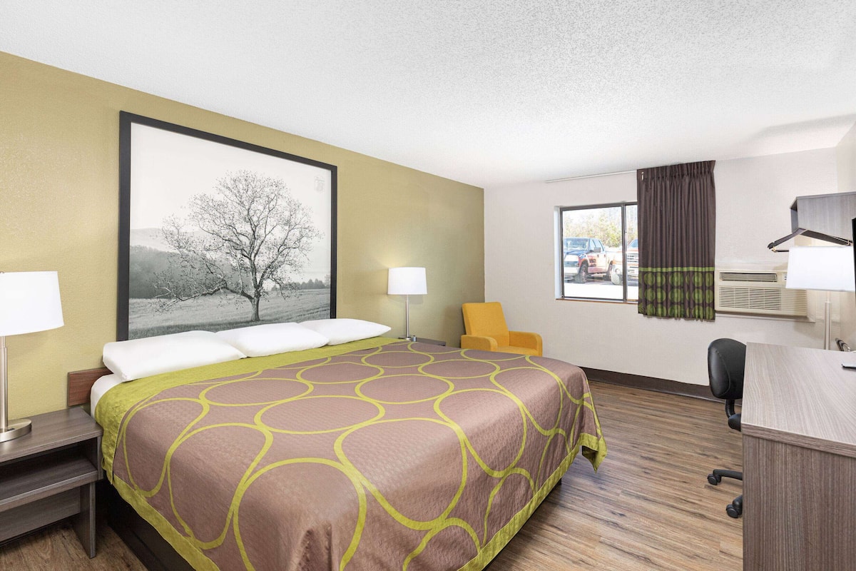 A hotel room with a large bed, a desk, a chair, and a window with curtains.