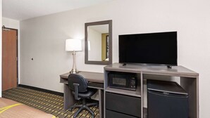 A hotel room with a desk, a chair, a television, a microwave, and a mini-fridge.
