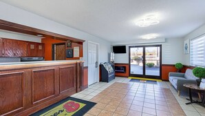 A hotel lobby with a reception desk, a sofa, a small table, a water dispenser, and a door leading outside.