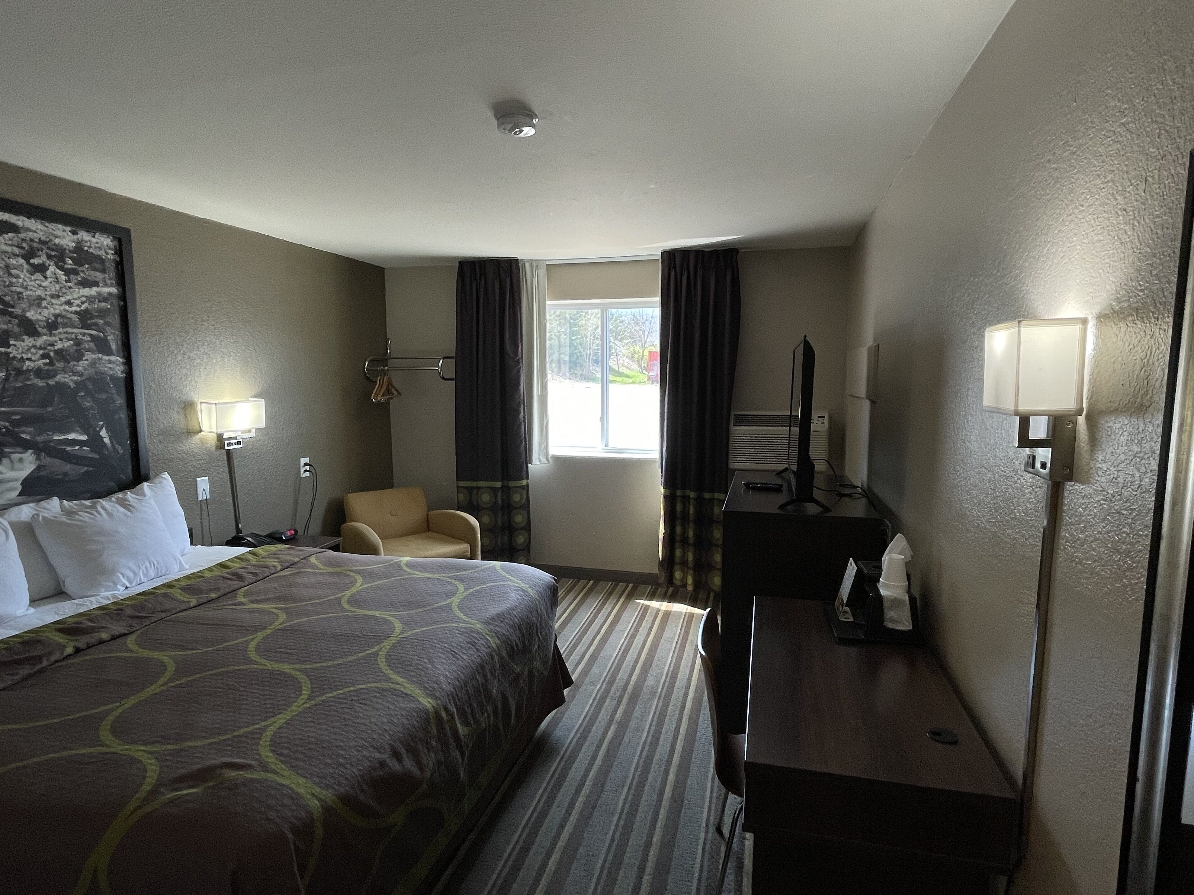 Une chambre d’hôtel avec un lit, un bureau, une chaise, une télévision et une fenêtre avec des rideaux.