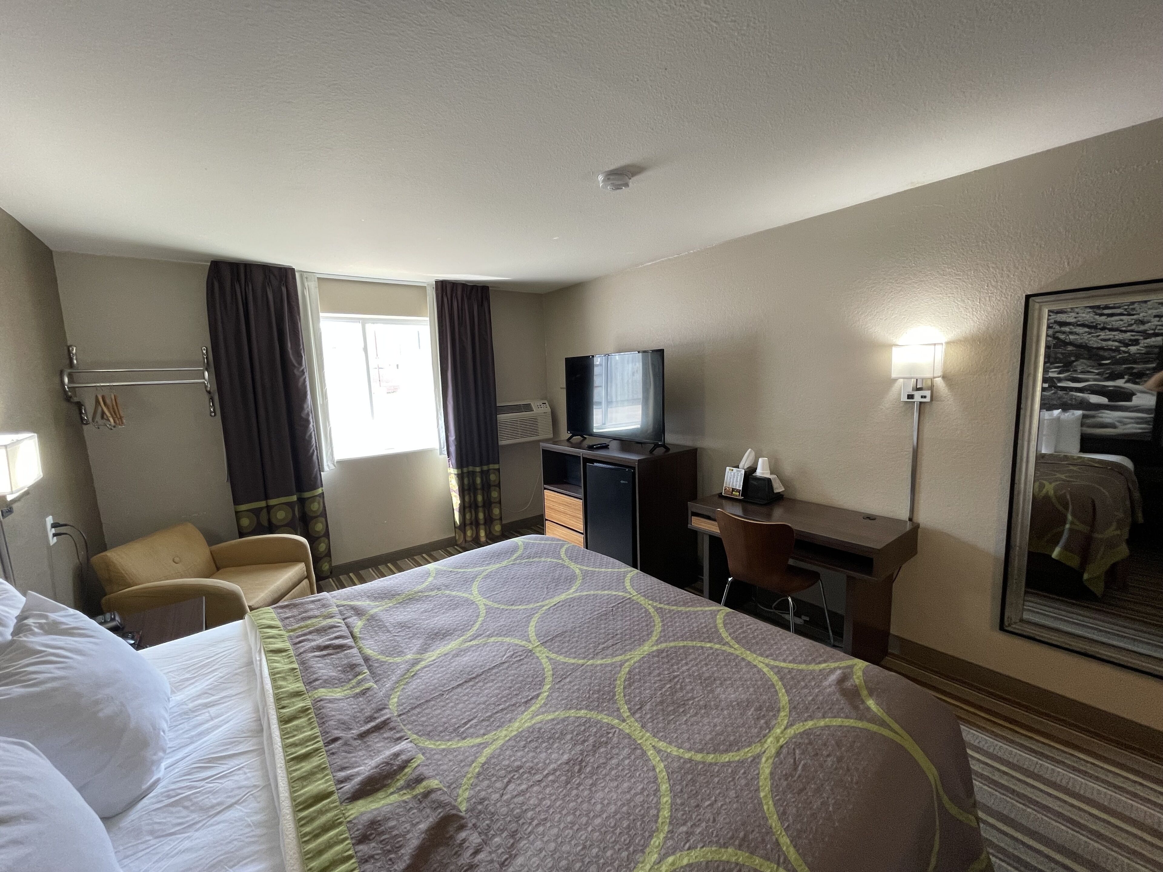 Habitación de hotel con cama, escritorio, silla, televisor y ventana con cortinas.