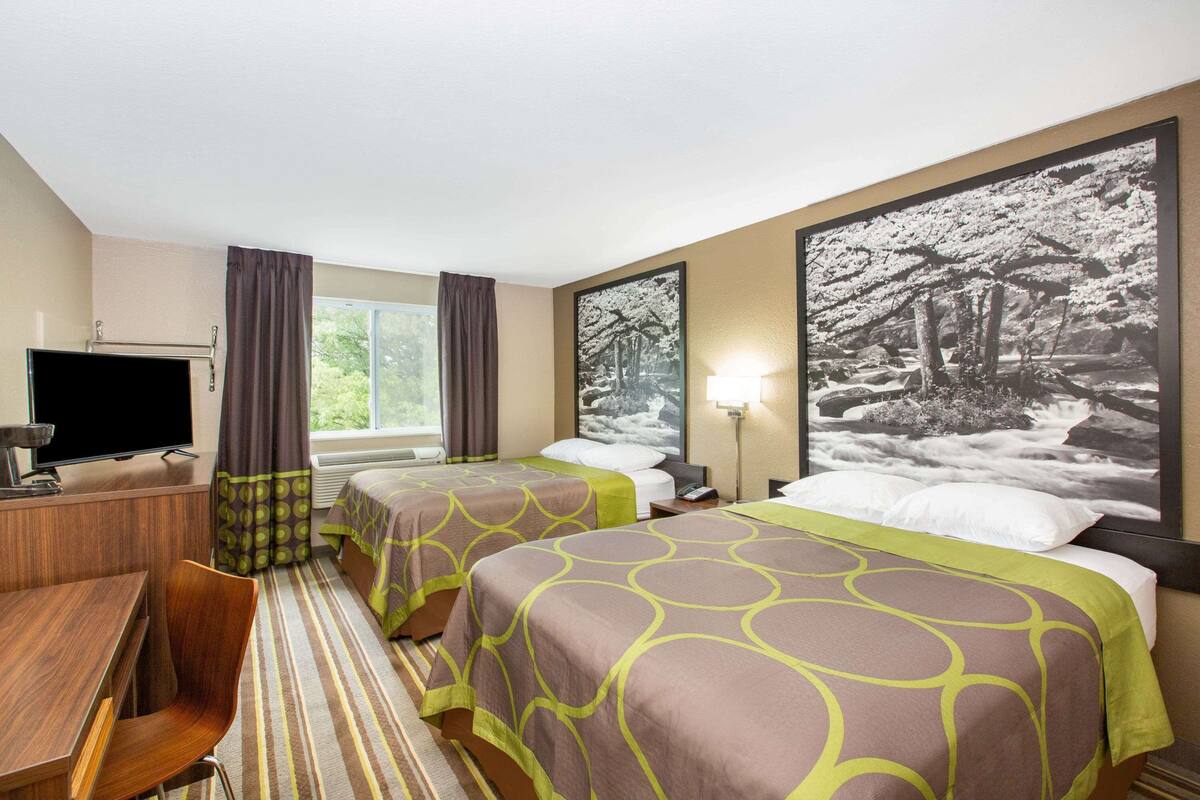 Habitación de hotel con dos camas, un escritorio, un televisor y grandes cuadros en las paredes.