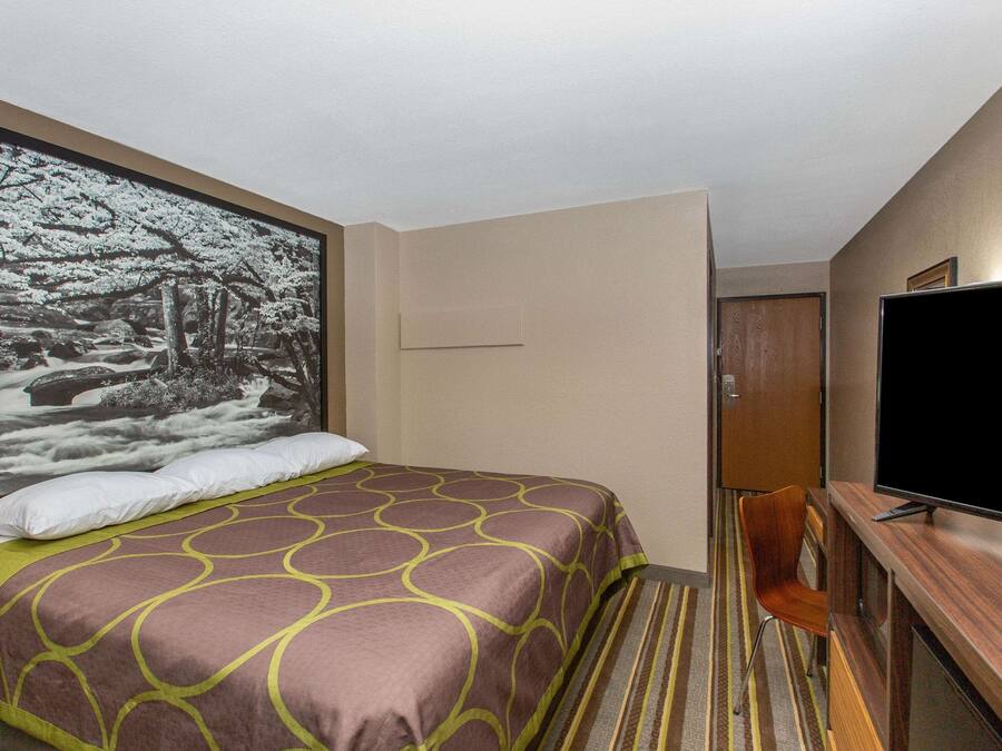 A hotel room with a bed, a television, a desk, and a large framed picture on the wall.