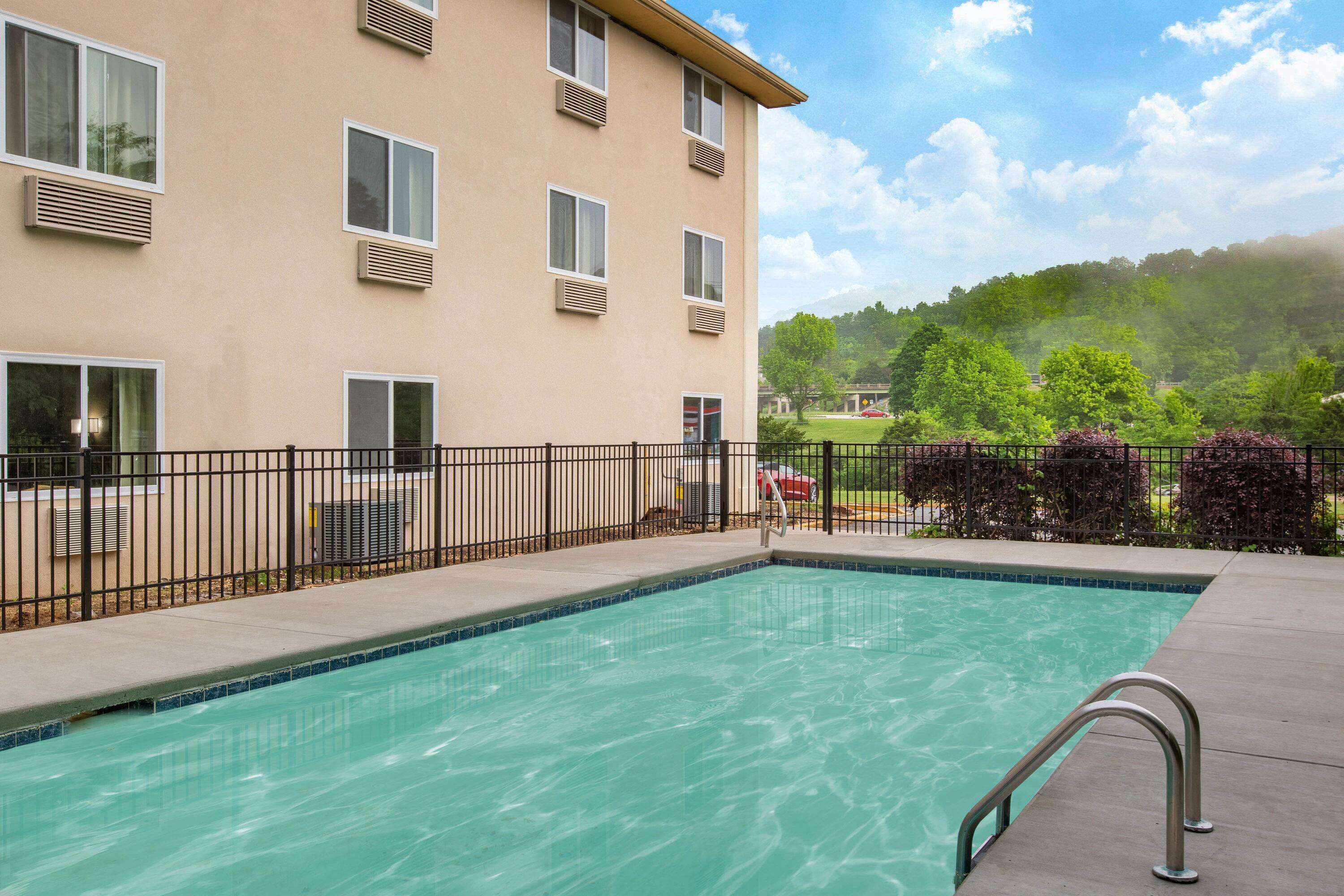 A swimming pool with a metal railing, a beige building with multiple windows, and a green landscape in the background.