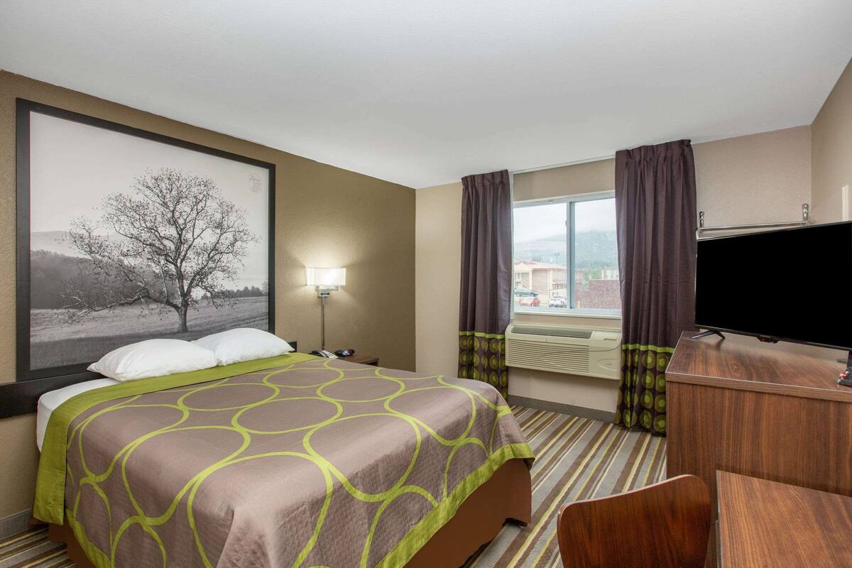 Una habitación de hotel con cama, escritorio, televisor y ventana con cortinas.