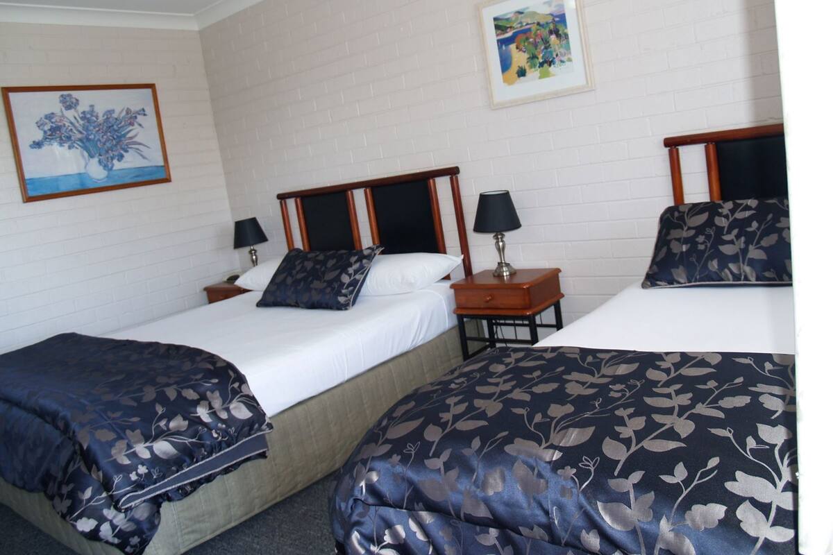 A hotel room with two beds, a nightstand with a lamp, and a framed painting on the wall.