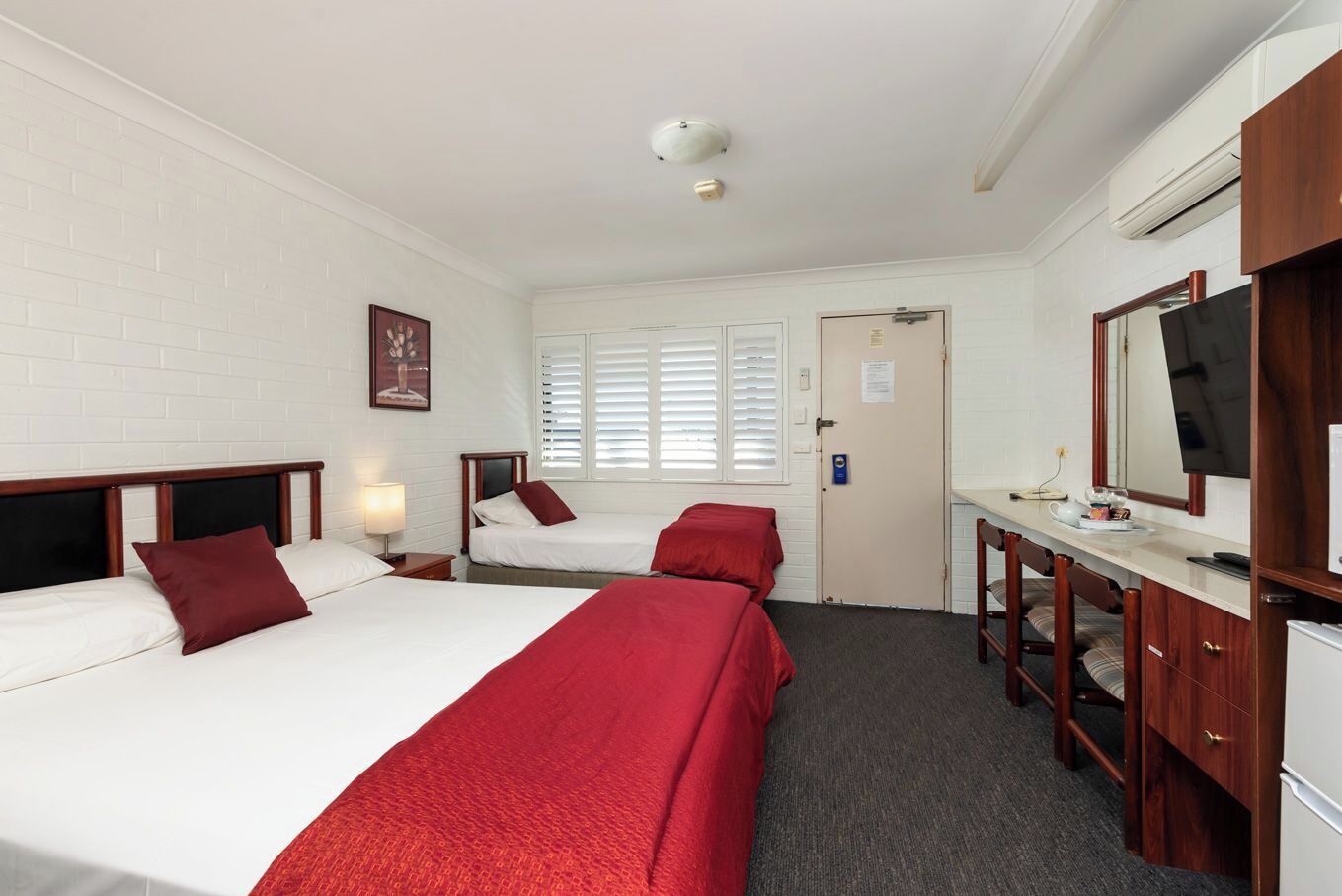 A hotel room with two beds, a desk with a mirror, and a television.
