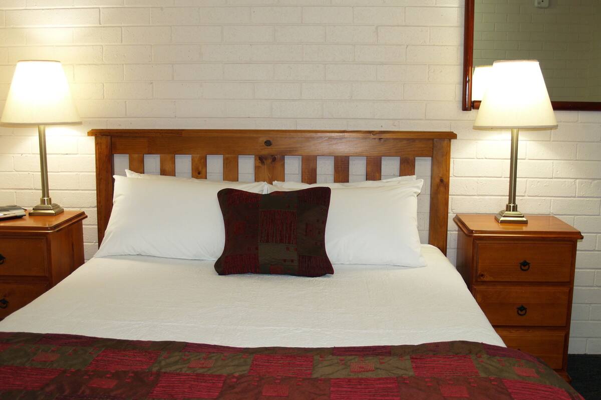 A neatly made bed with a quilt, two bedside lamps, a wooden headboard, and a nightstand with a drawer.