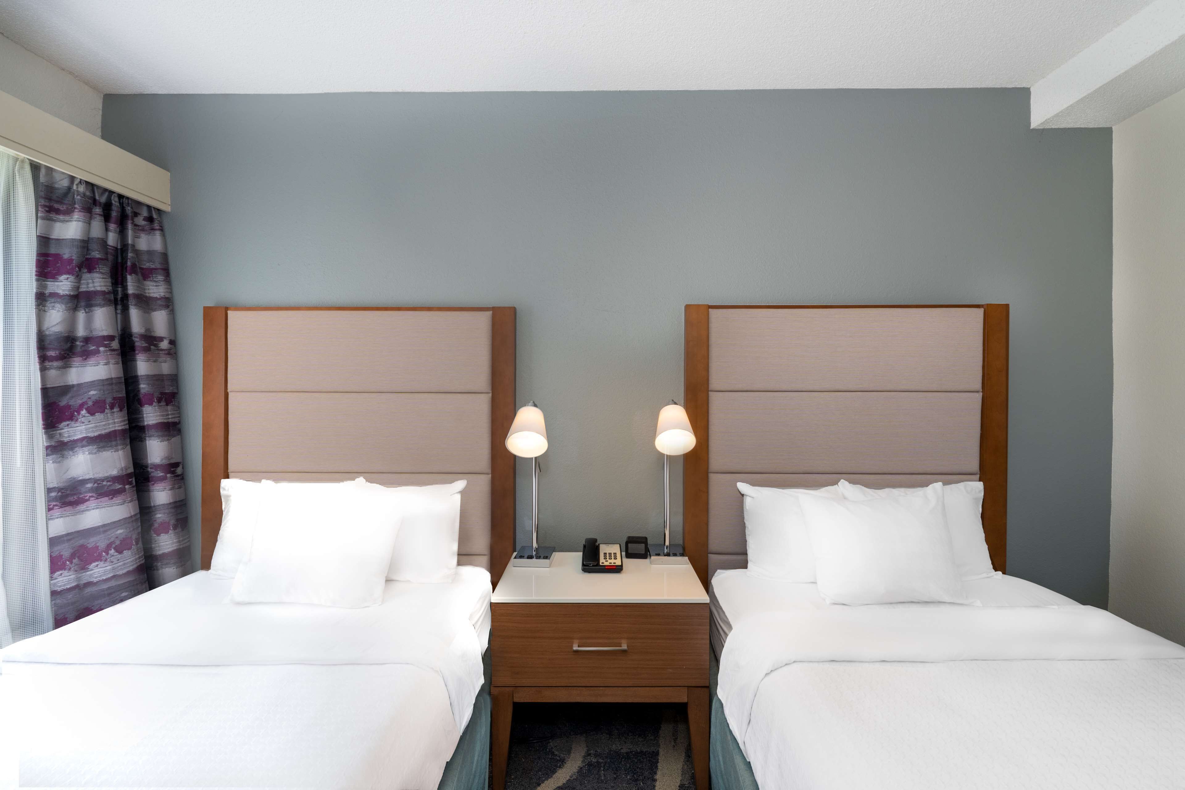 A hotel room with two single beds, a wooden nightstand between them, a small drawer, and a telephone.