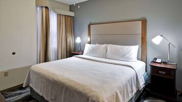 A hotel room with a large bed, two bedside tables with lamps, a window with curtains, and a carpeted floor.