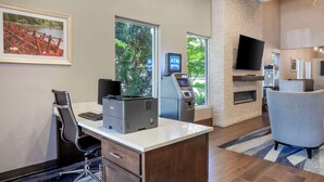 A modern hotel room with a desk, printer, ATM, and a fireplace.