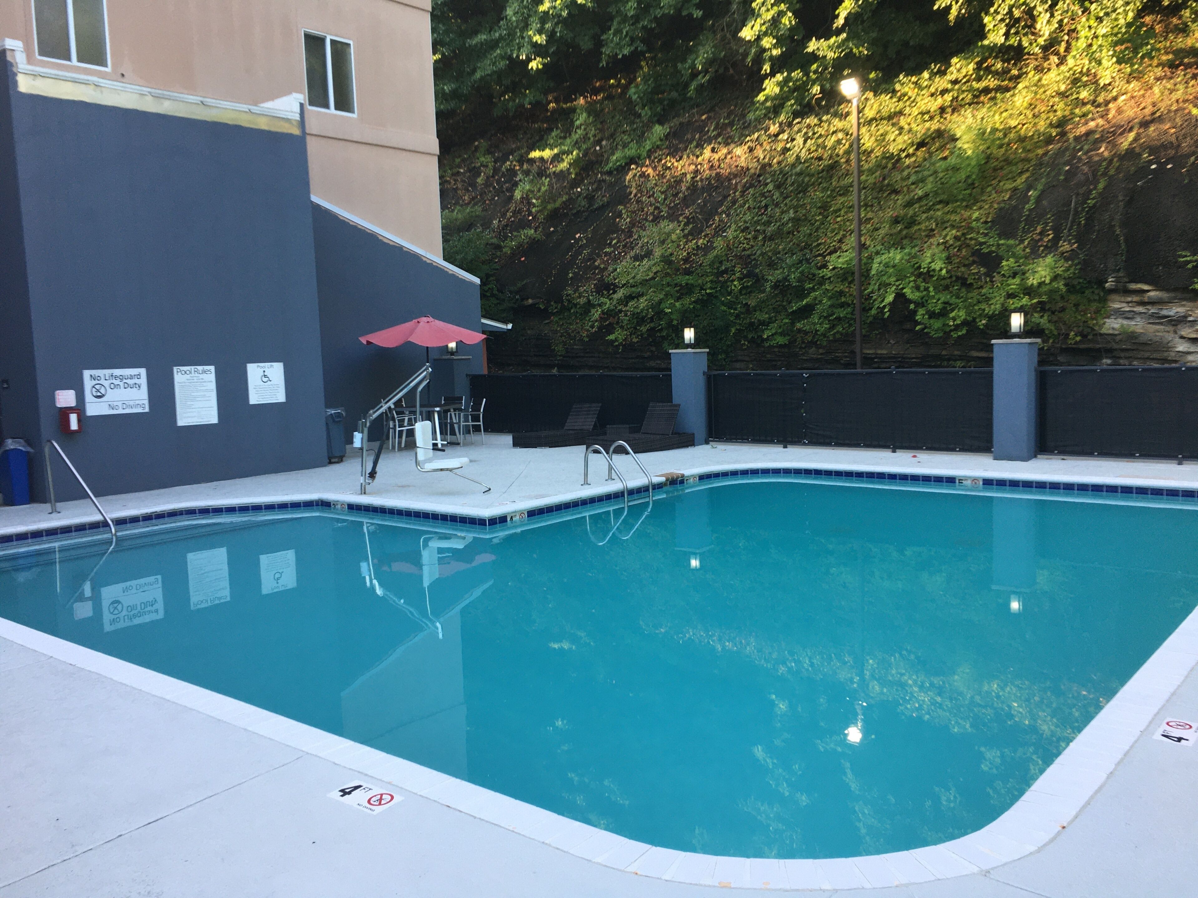 A swimming pool with a tiled edge, a red umbrella, and a chair.