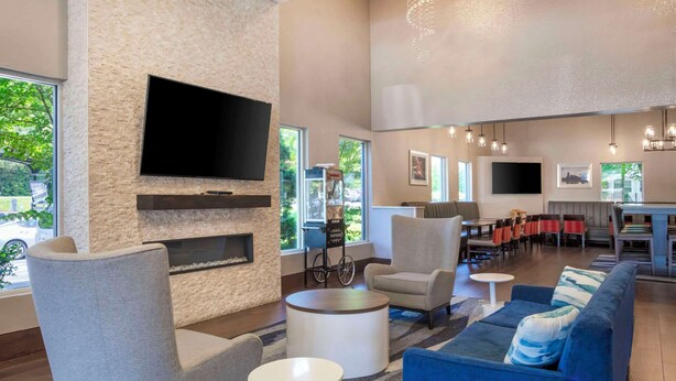 A modern lobby with a flat-screen TV, comfortable seating, a fireplace, and large windows offering a view of the outdoors.