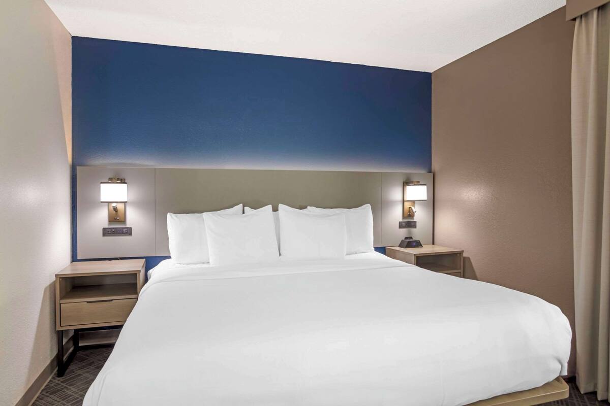 A hotel room with a large bed, two bedside tables, and wall-mounted lamps.