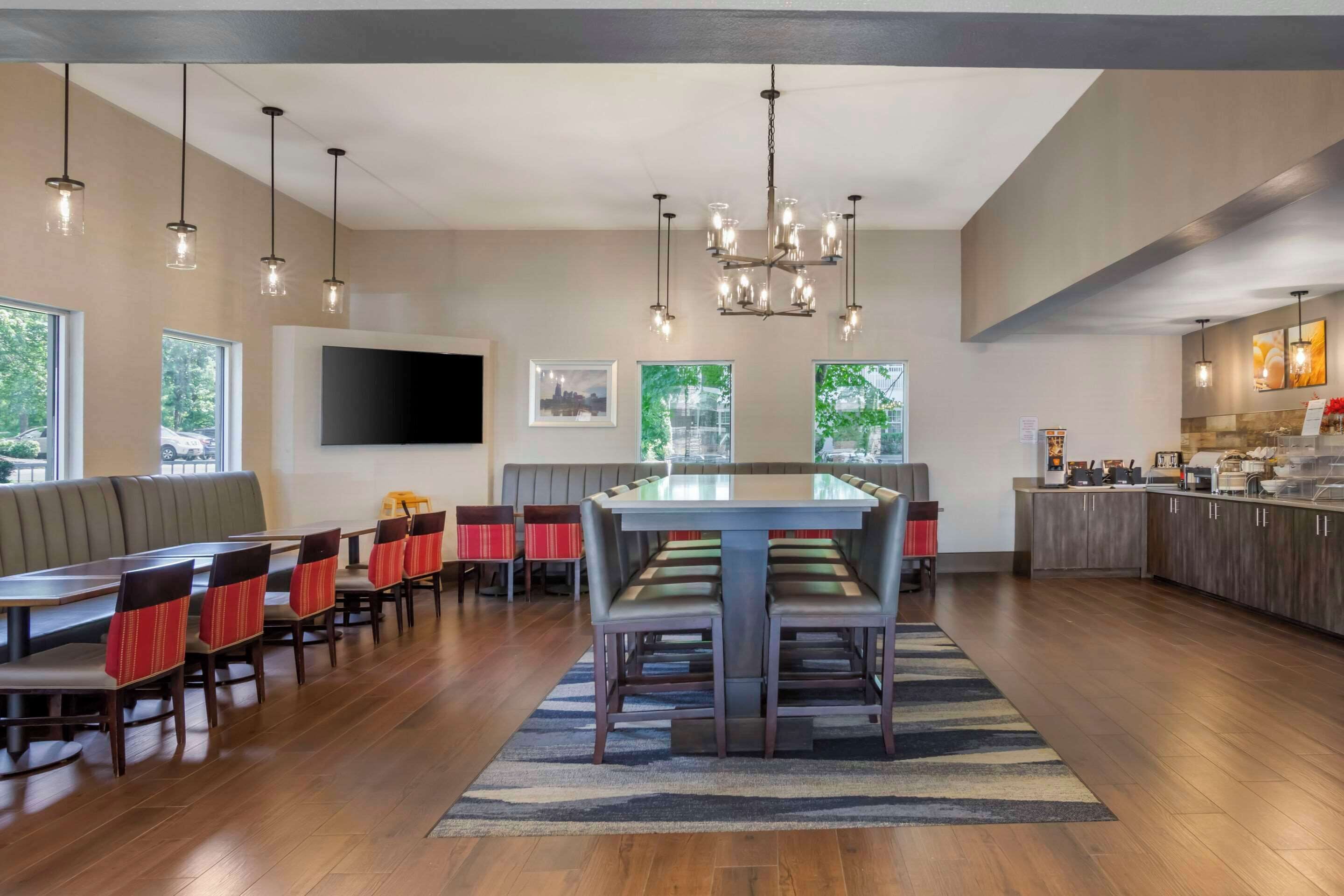A spacious dining area with a long table and multiple chairs, a bar area with a counter and stools, and a large window providing a view of greenery.