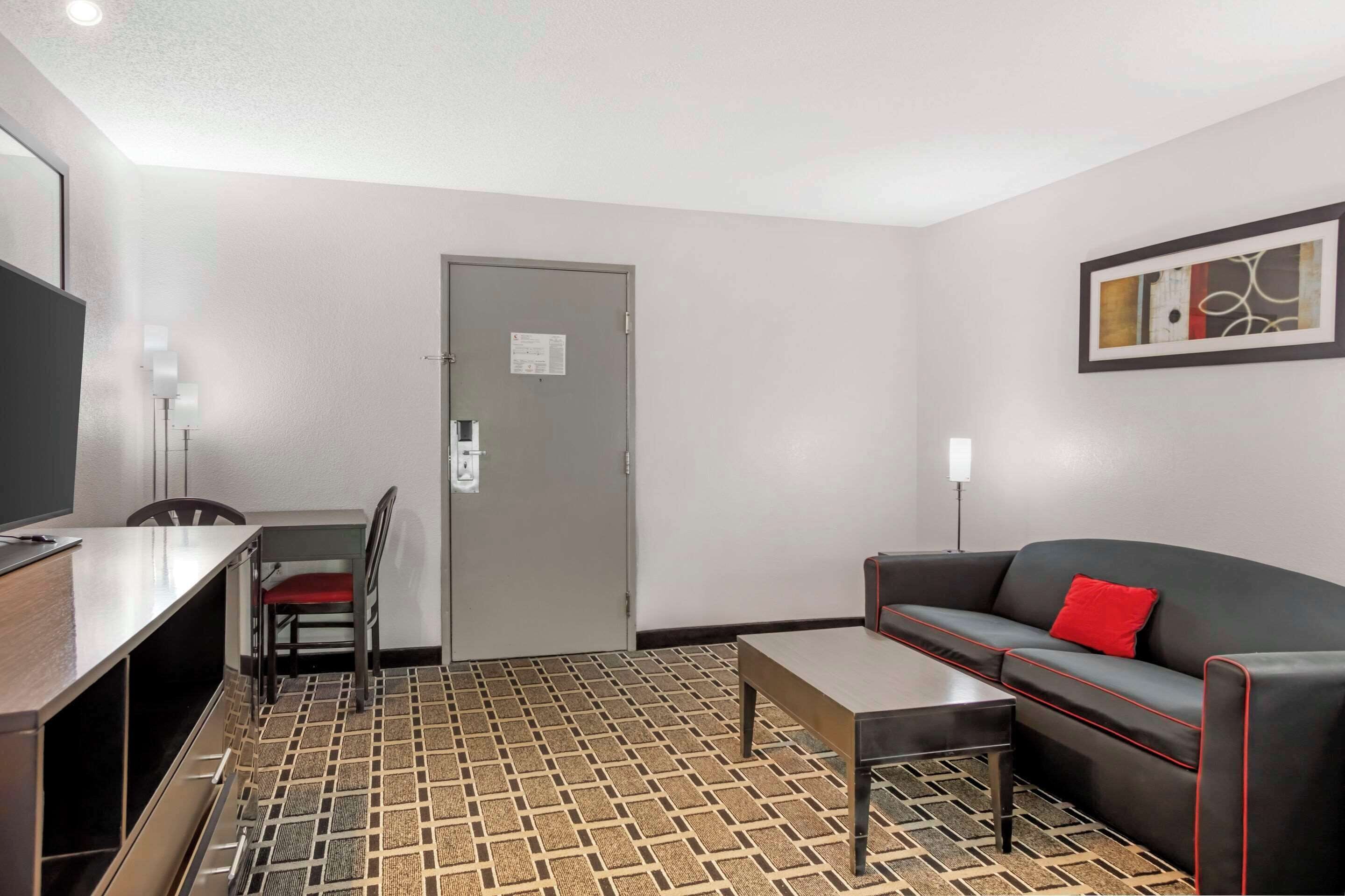 Una habitación de hotel con una mesa de comedor, un sofá, un televisor y una puerta con un letrero.