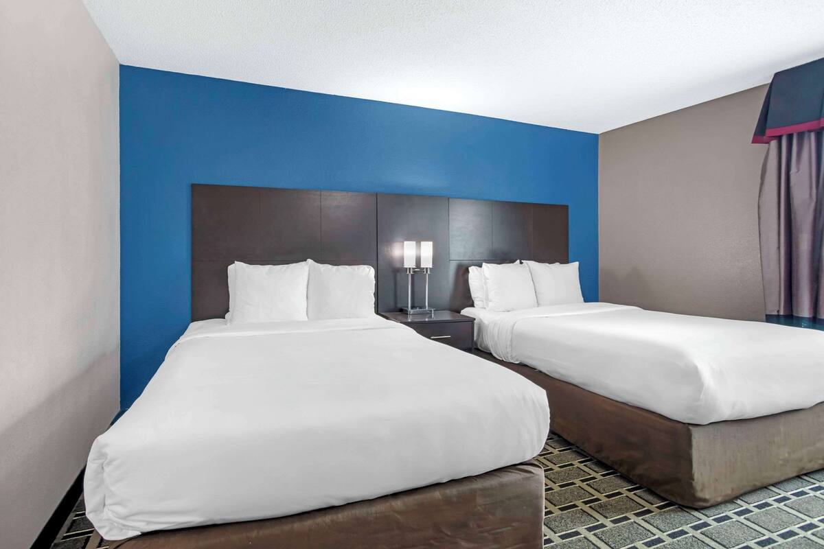 A hotel room with two single beds, a dark headboard, a nightstand with a lamp, and a patterned floor.