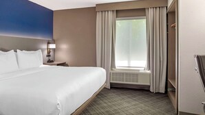 A hotel room with a large bed, a nightstand, a lamp, a window with curtains, and an air conditioning unit.