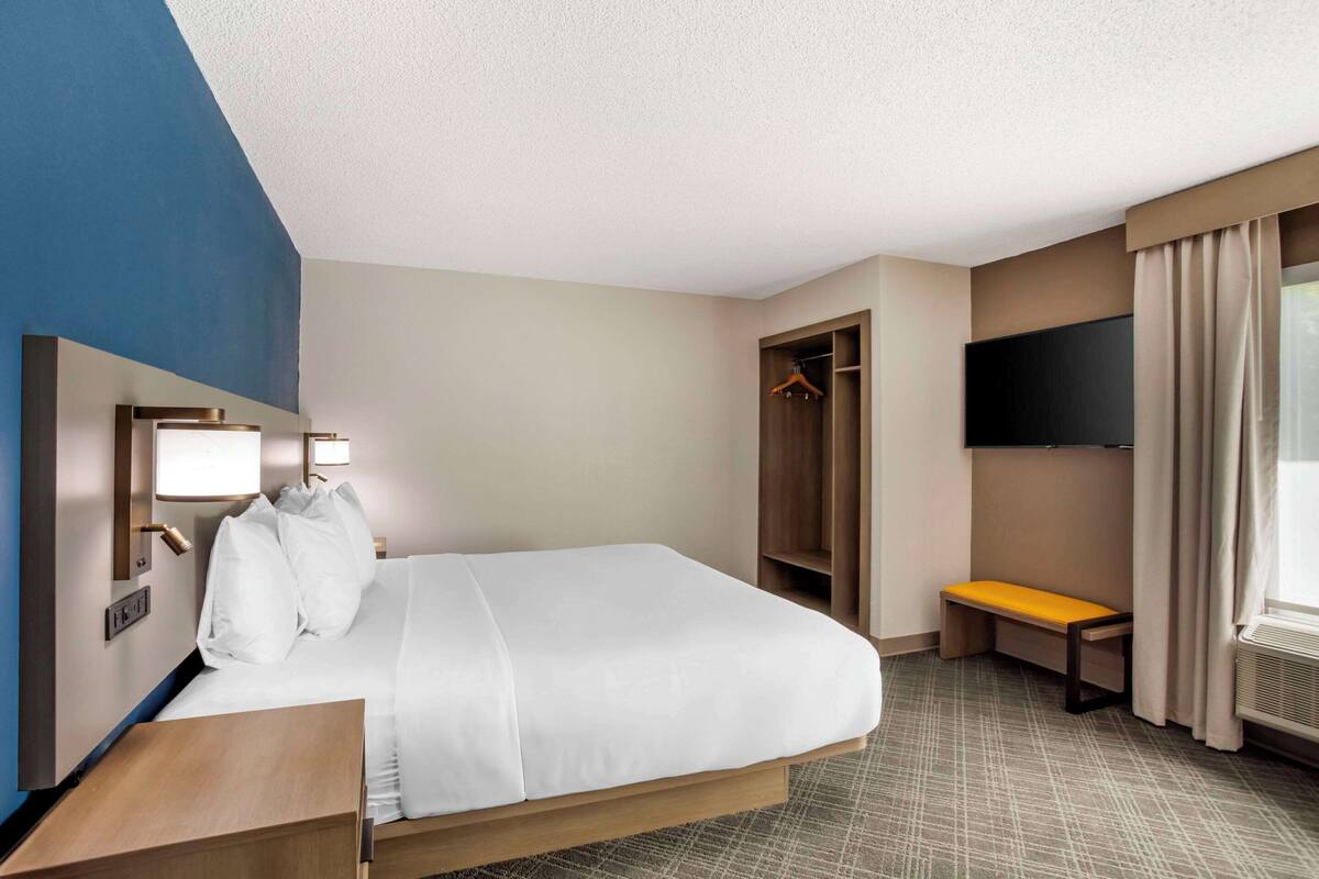 A hotel room with a bed, a bench, a wardrobe, a TV, and a window with curtains.