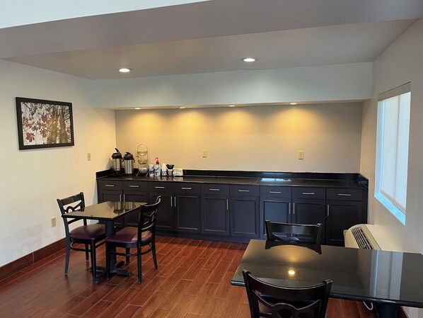 A modern kitchen with dark cabinets, a dining table, and chairs. There is a window providing natural light and a wall-mounted picture. - Red Roof Inn Kimball, TN - I-24 (Jasper)