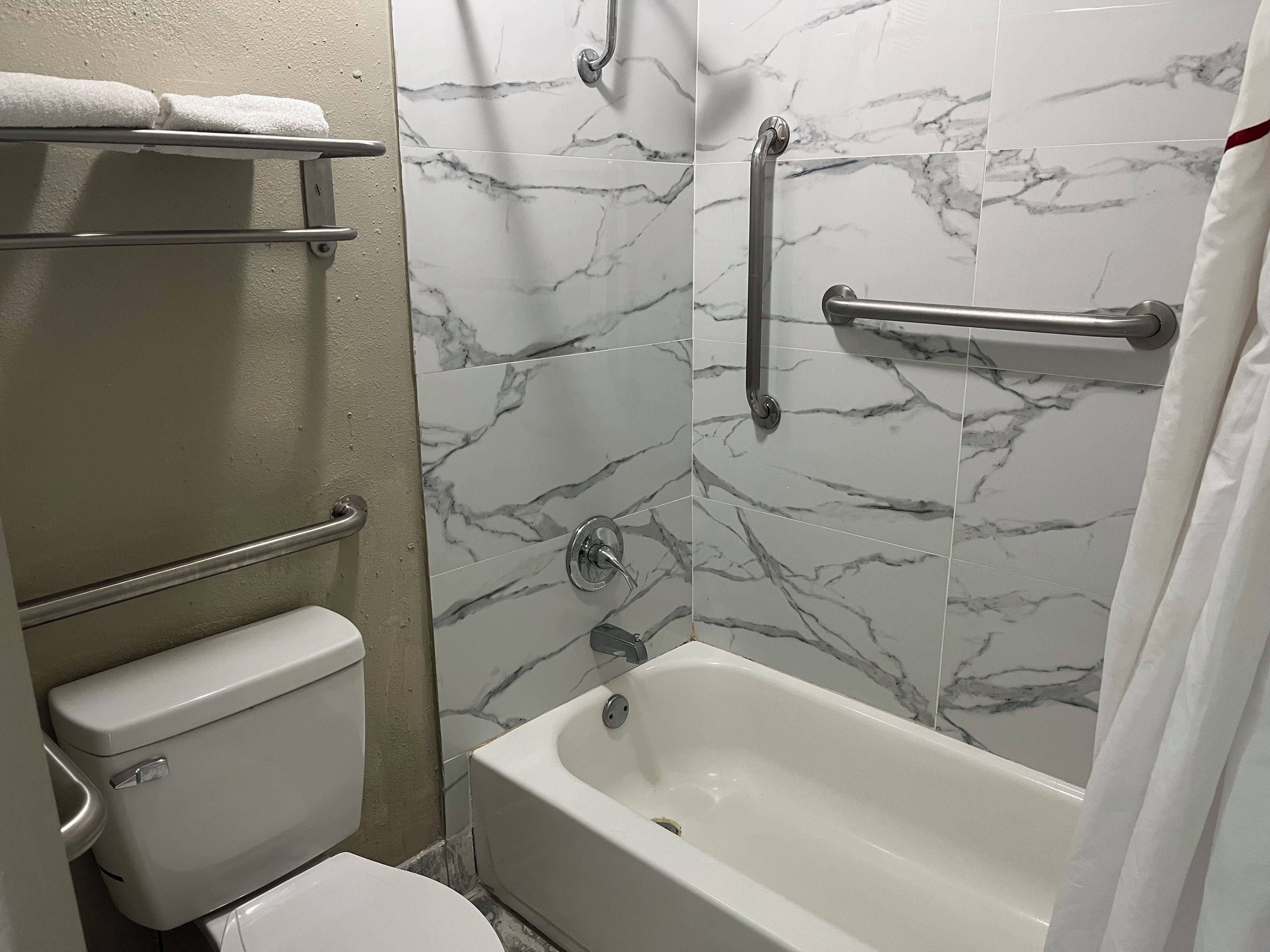 A bathroom with a bathtub, toilet, and handrails.