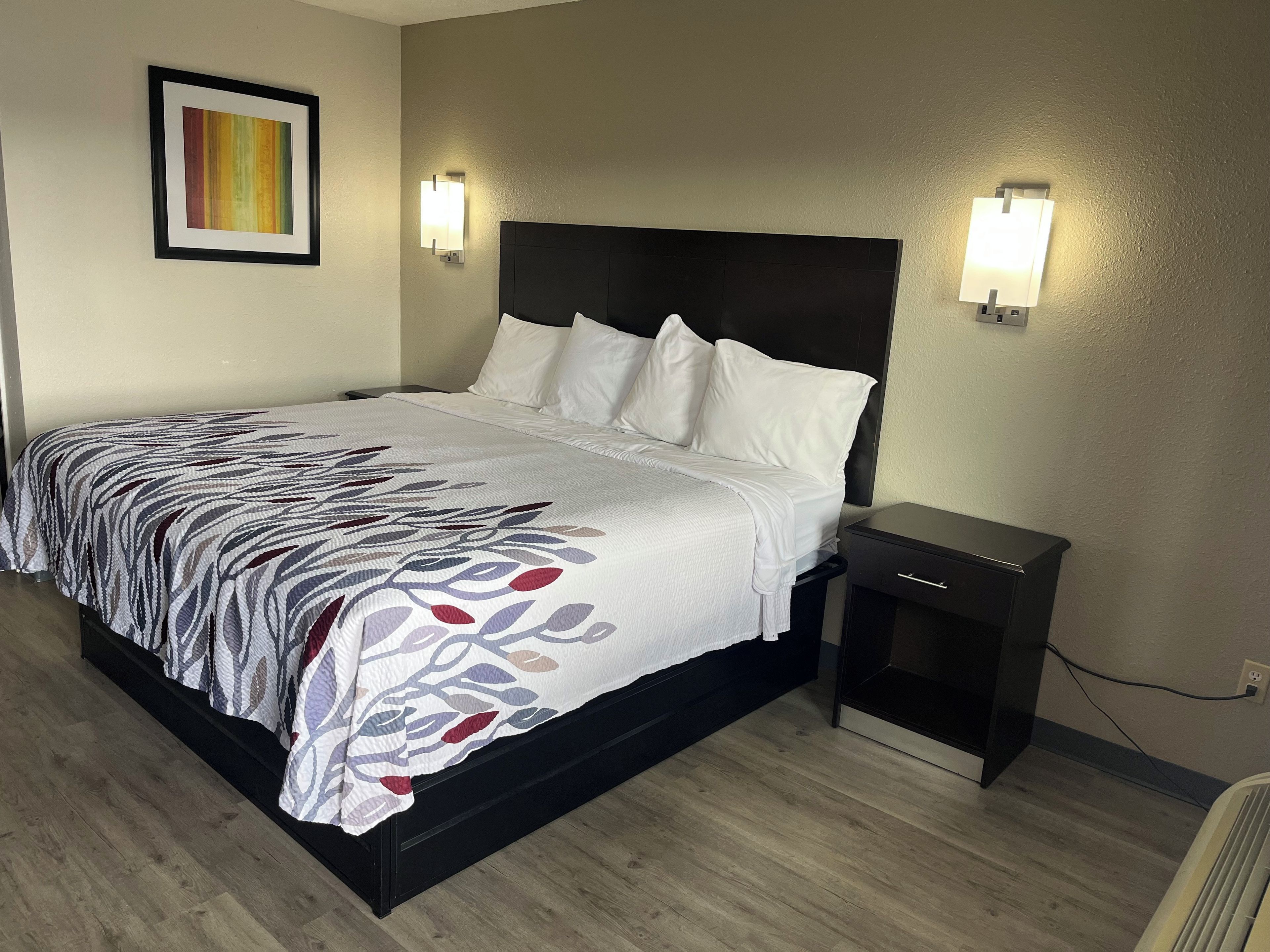 A neatly made bed with a patterned bedspread, two bedside lamps, a small nightstand, and a framed picture on the wall.