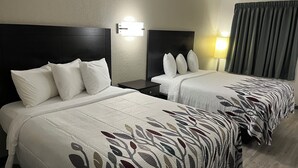 A hotel room with two beds, each with white bedding and a leaf-patterned duvet cover. There is a nightstand with a lamp between the beds, and a window with curtains. - Red Roof Inn Kimball, TN - I-24 (Jasper)