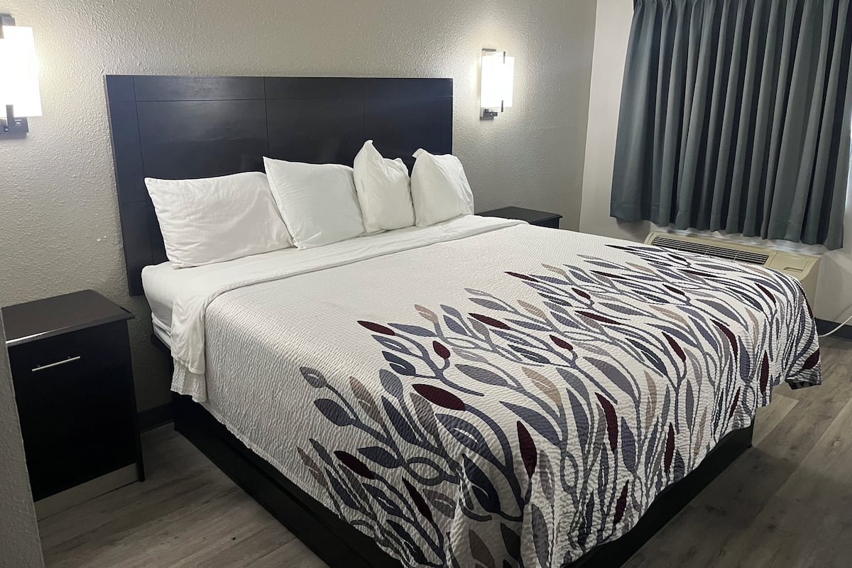A neatly made bed with a patterned bedspread, a dark headboard, and two bedside tables.