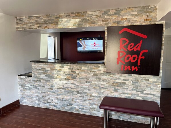 A reception area with a stone wall, a television displaying Red Roof Inn, and a bench. - Red Roof Inn Kimball, TN - I-24 (Jasper)