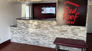 A reception area with a stone wall, a television displaying Red Roof Inn, and a bench. - Red Roof Inn Kimball, TN - I-24 (Jasper)