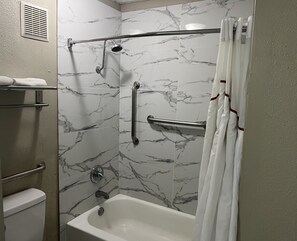 A bathroom with a bathtub, a shower with a handheld showerhead, grab bars, and a towel rack. - Red Roof Inn Kimball, TN - I-24 (Jasper)