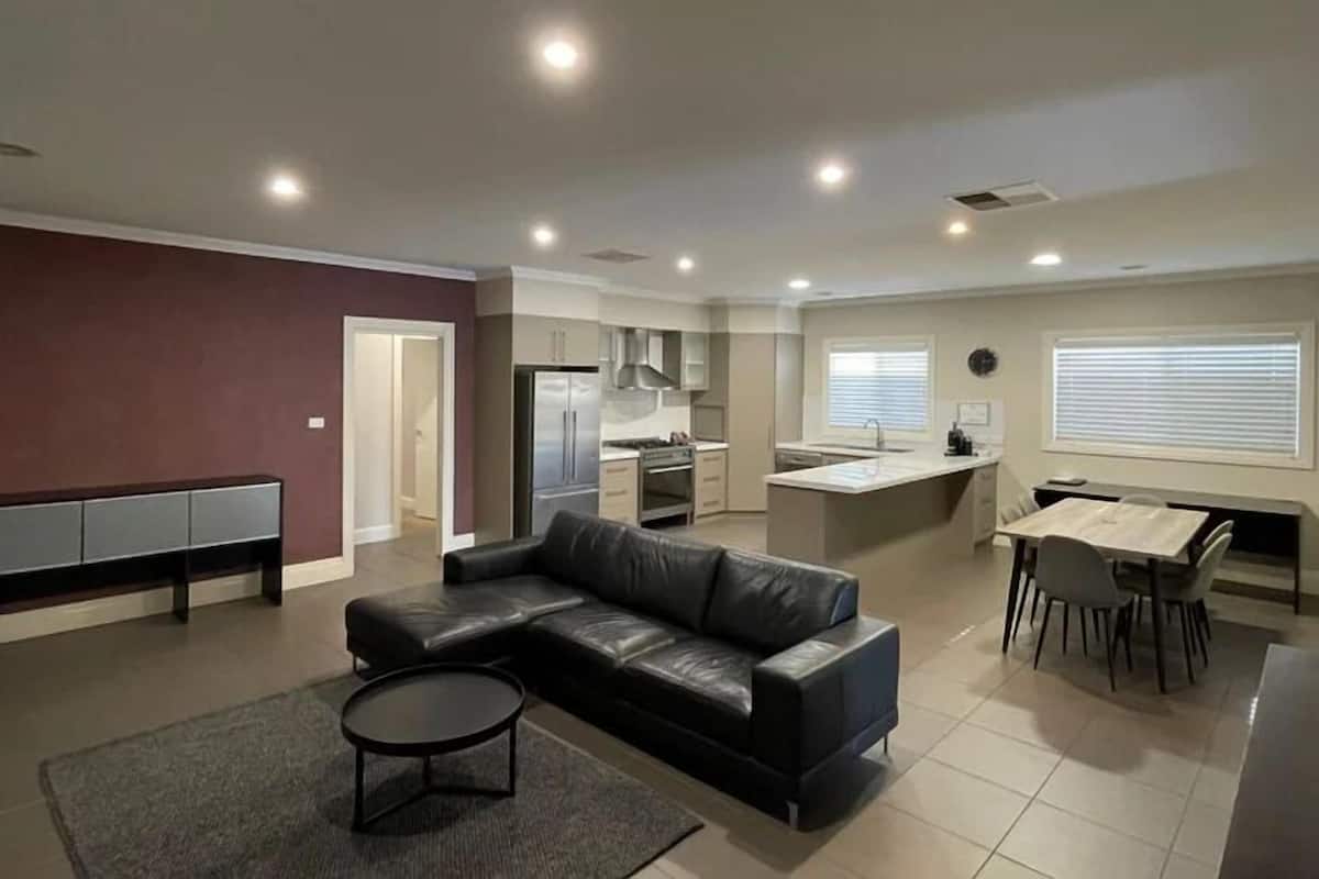 A modern living room with a black leather sofa, a round coffee table, and a dining area with a small island and chairs.