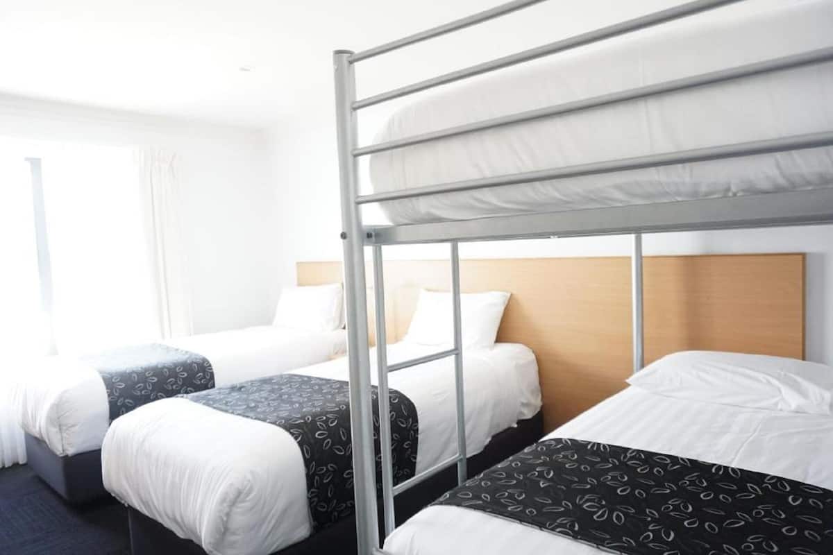 A hotel room with bunk beds, a wooden headboard, and a window with curtains.