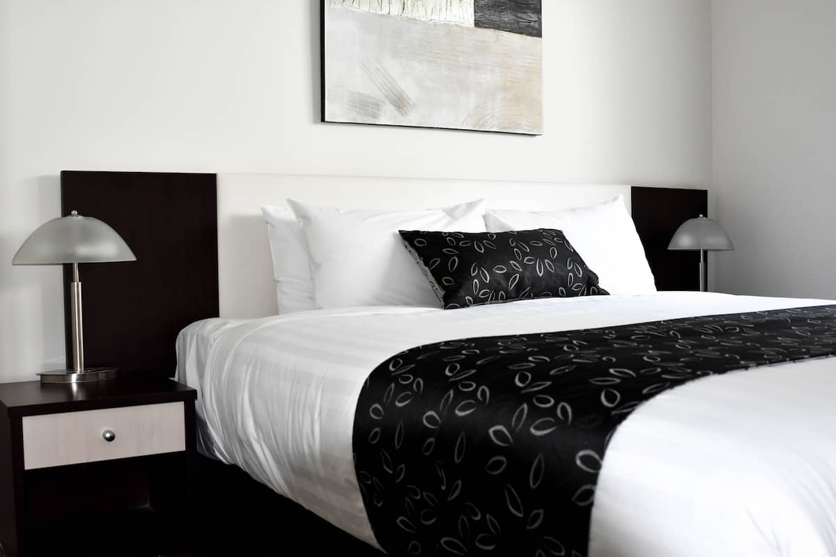 A neatly made bed with a black and white patterned throw, two bedside lamps, and a minimalist artwork above the bed.