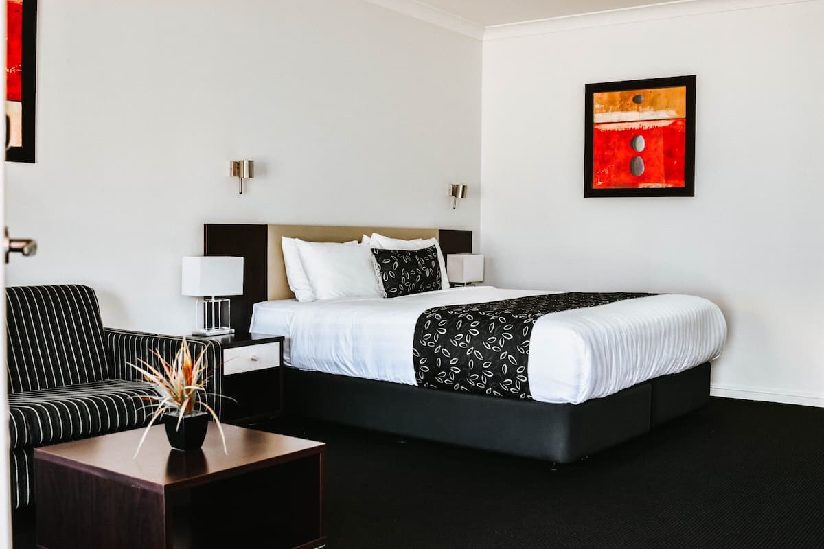 A hotel room with a bed, a sofa, a nightstand, and a wall-mounted artwork.