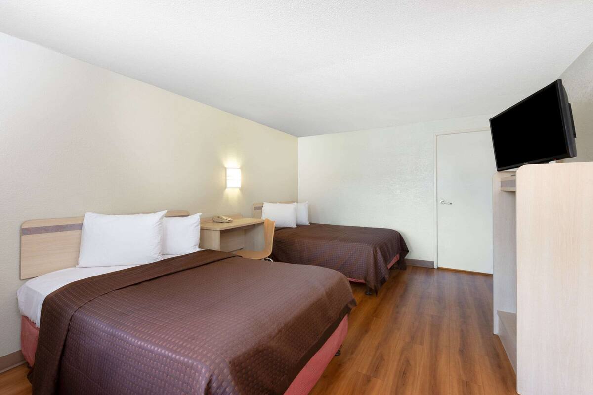 Habitación de hotel con dos camas, un escritorio con silla, televisión y una lámpara fijada a la pared.