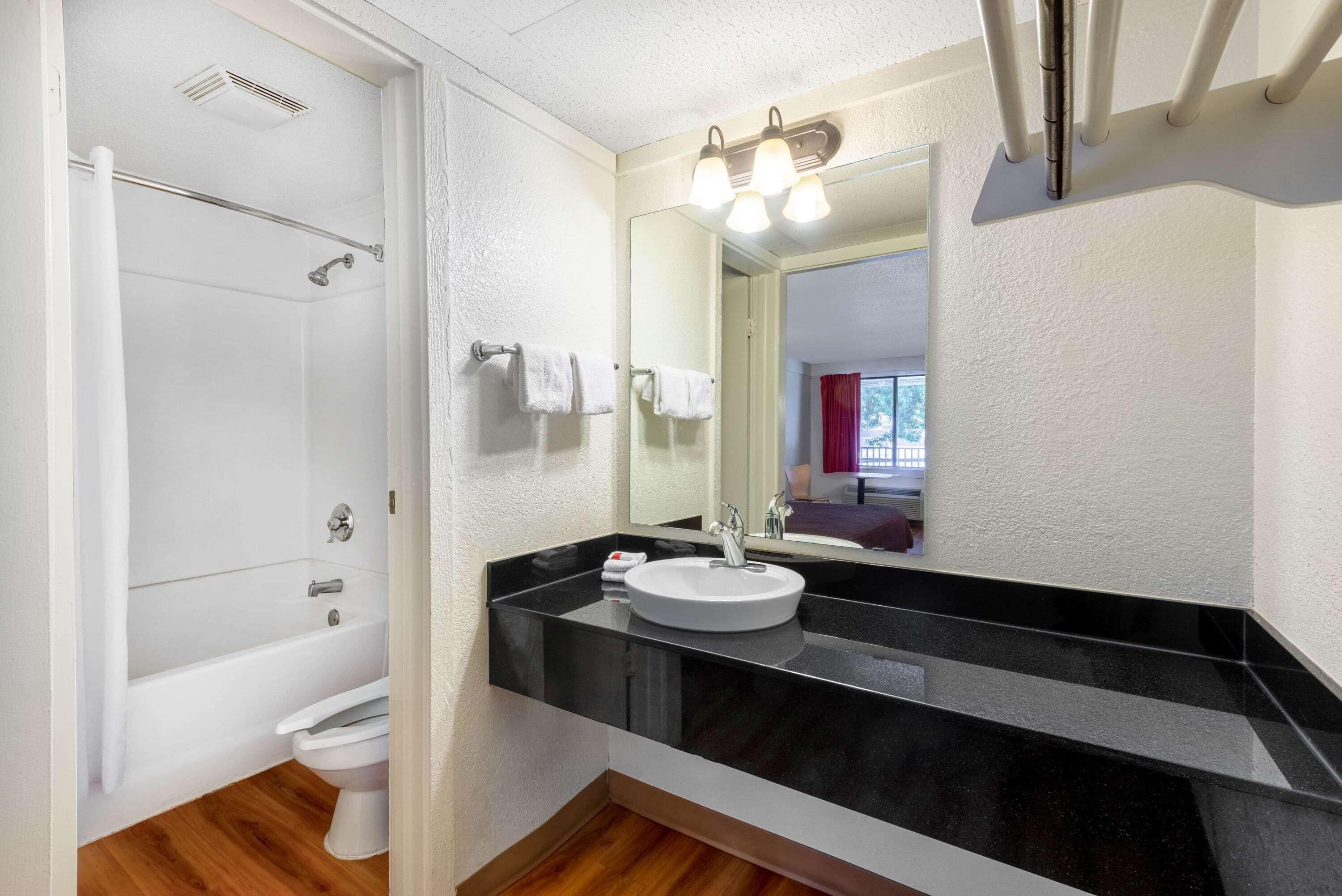 A modern bathroom with a white bathtub, a white toilet, a black countertop, and a large mirror.