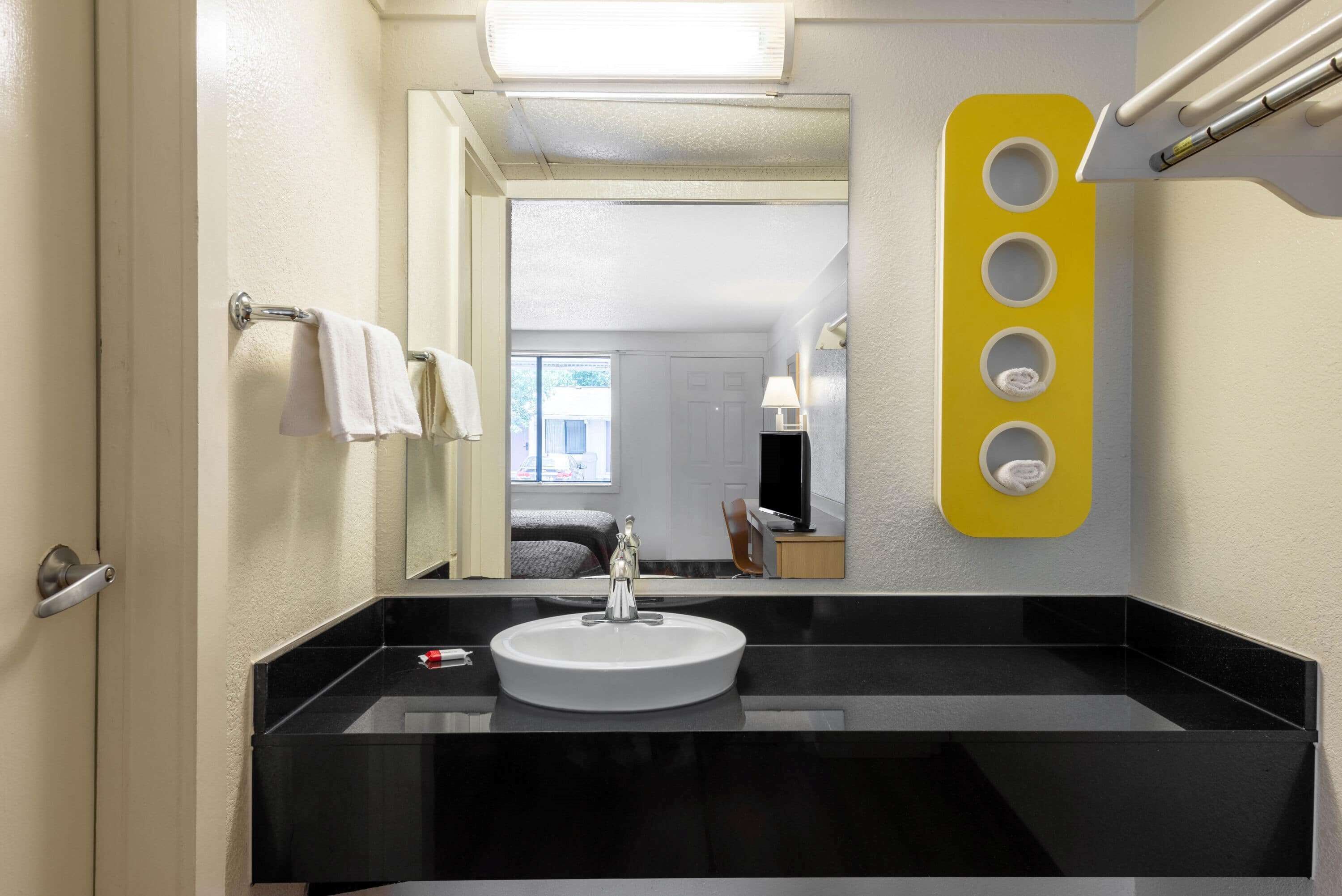 A modern bathroom with a black countertop sink, a mirror, and a yellow soap dispenser.
