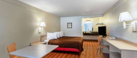 A hotel room with a bed, a desk, a chair, a TV, and a lamp.