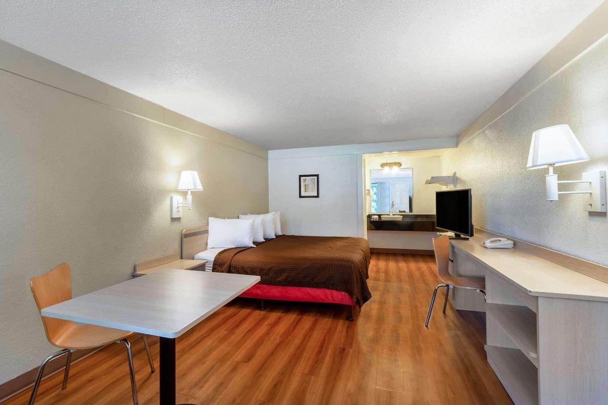 Una habitación de hotel compacta con cama, escritorio, silla, televisor y una mesita.