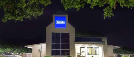 Un hôtel Travelodge de nuit, avec une enseigne bien visible, une entrée bien éclairée et des espaces verts aménagés.