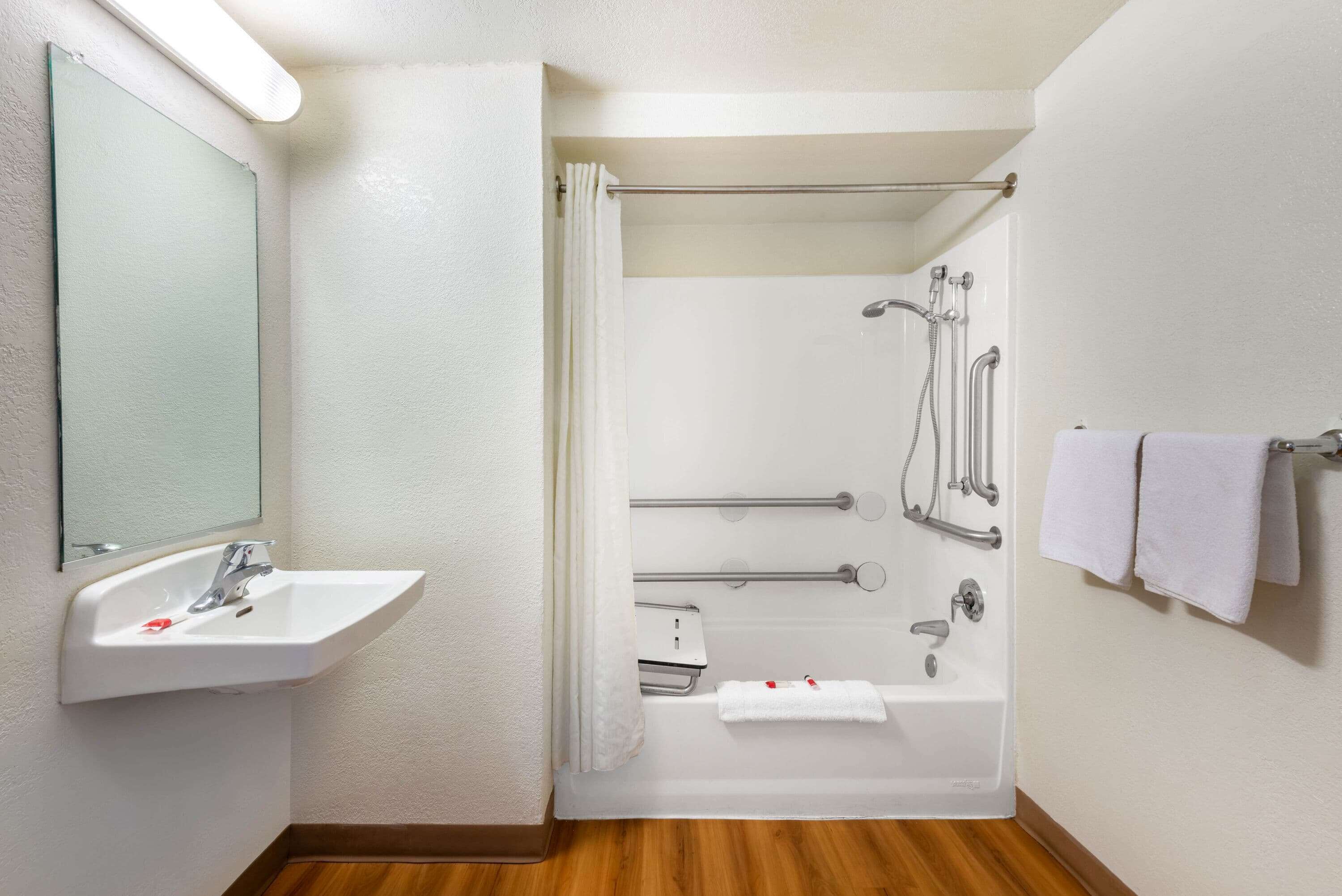 A bathroom with a sink, mirror, shower, and towel rack.