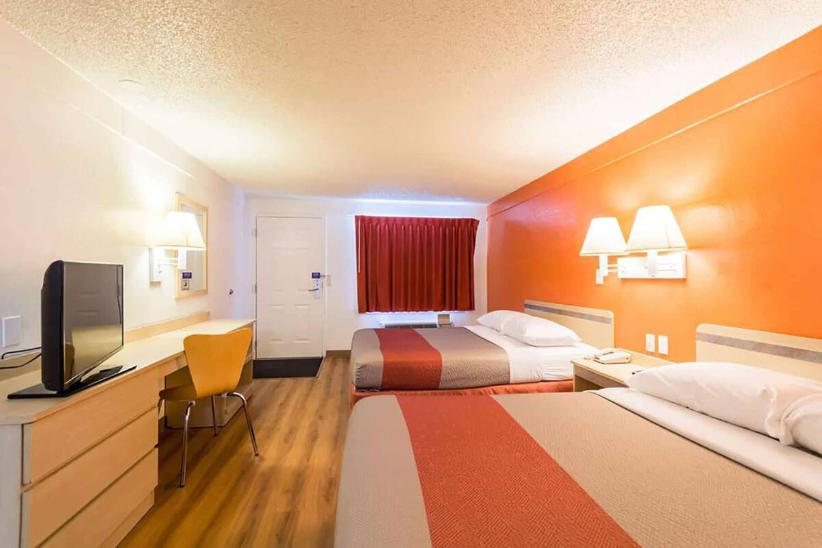 Una habitación de hotel con escritorio, dos camas, televisión y cortina roja.