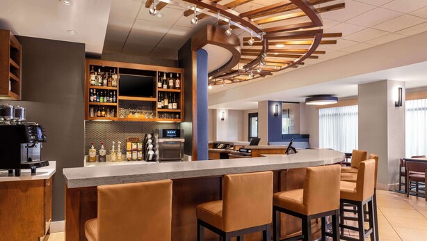 A modern bar area with a bar counter, seating, and a variety of liquor bottles.